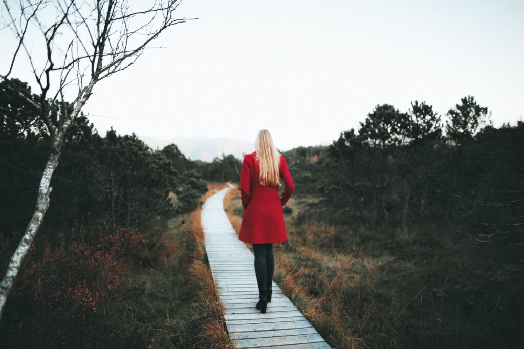 Woman in a red coat walking alone along a wooden boardwalk