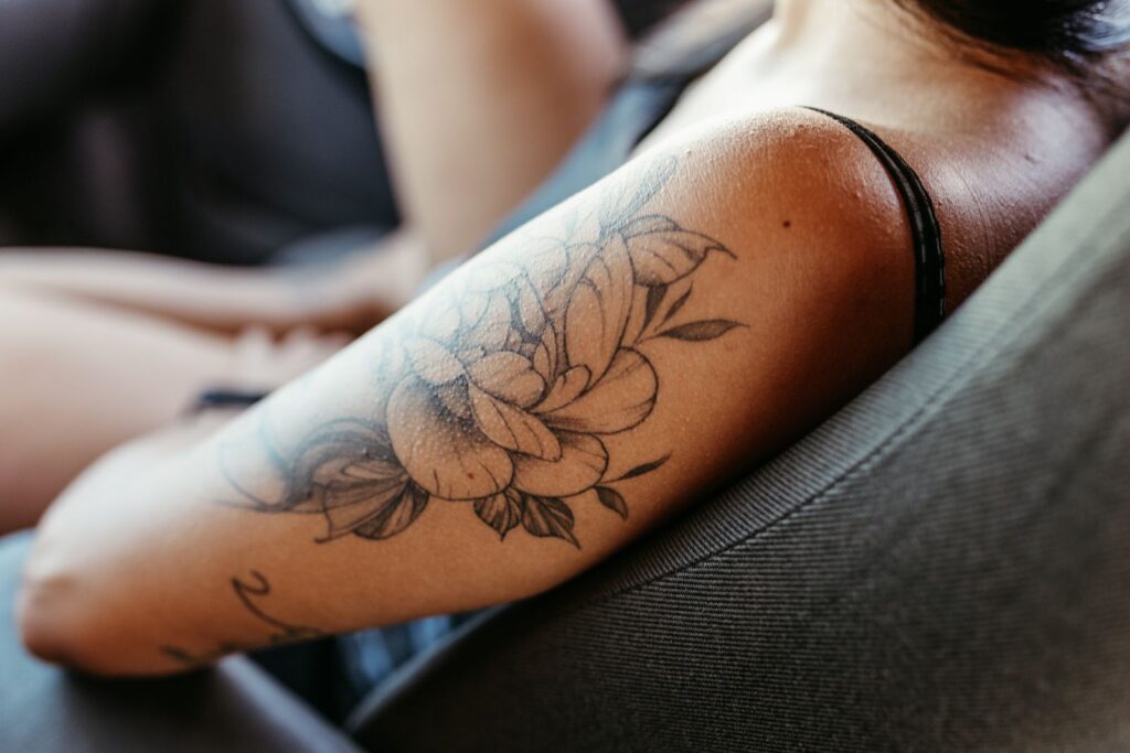 Fine line floral tattoo of peonies and leaves on a woman's upper arm
